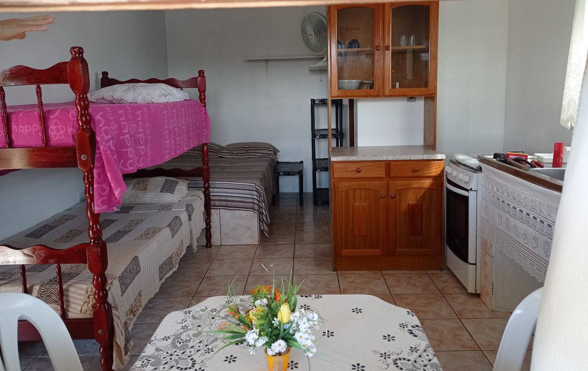 Interior de uma unidade da pousada com beliche, cama, armário de cozinha, fogão e mesa com flores
